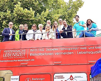 Mehrere Menschen stehen auf dem offenen Deck eines roten Doppeldeckerbusses