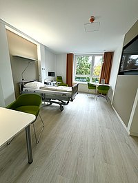 Blick in eine Krankenhaus-Einzelzimmer mit hellem Boden und grünen Sesseln