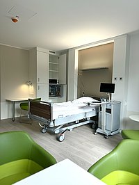 Blick in ein Krankenhaus-Einzelzimmer mit hellem Boden und grünen Sesseln